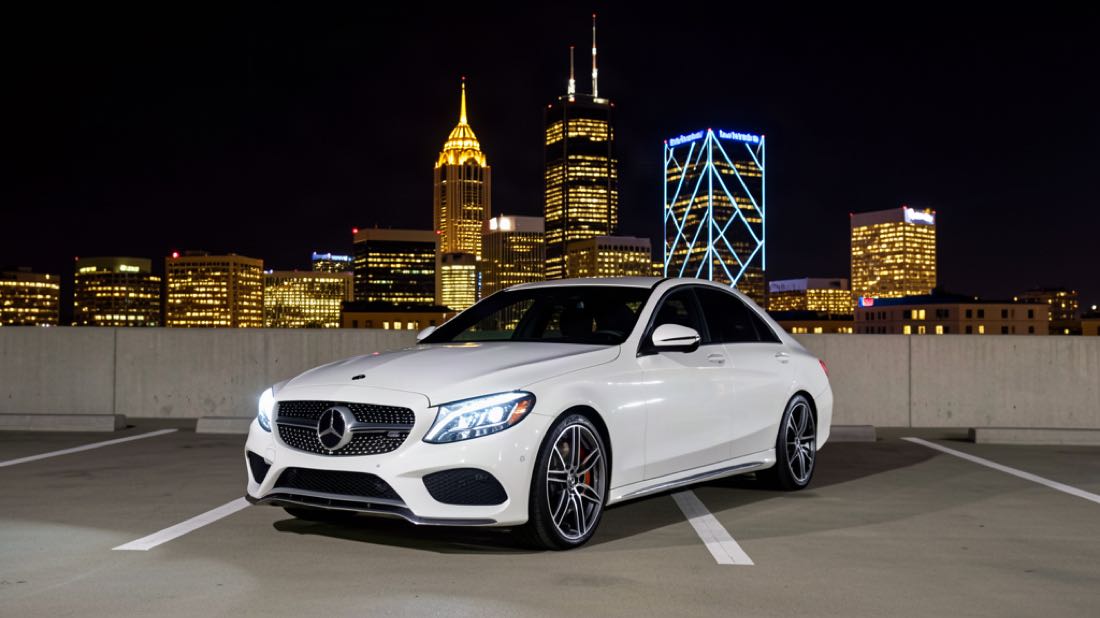 White 2017 Mercedes-Benz C300 sedan on a rooftop parking deck with the Charlotte skyline at night